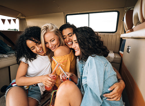 Group of four young women cuddling each other while sitting in van enjoying vacation