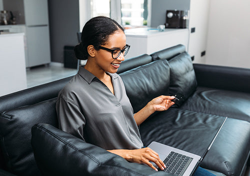 Cheerful young woman using a credit card and laptop computer to shop online from home