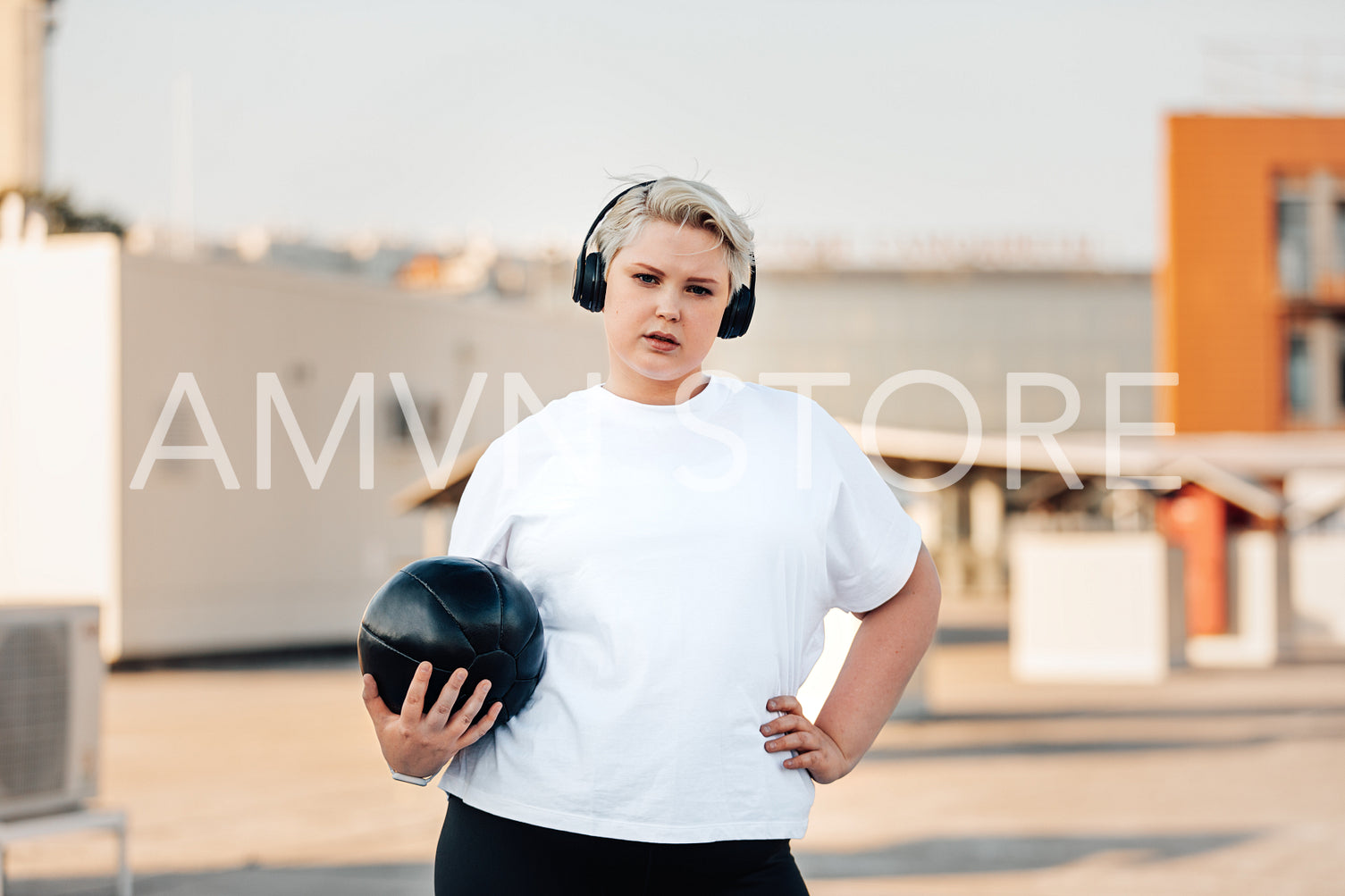 Young woman with plus size body holding a medicine ball while standing on a roof	