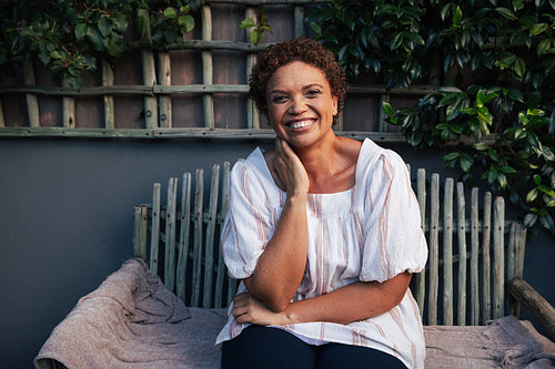 Smiling senior woman in casuals looking at camera while sitting outside in the backyard