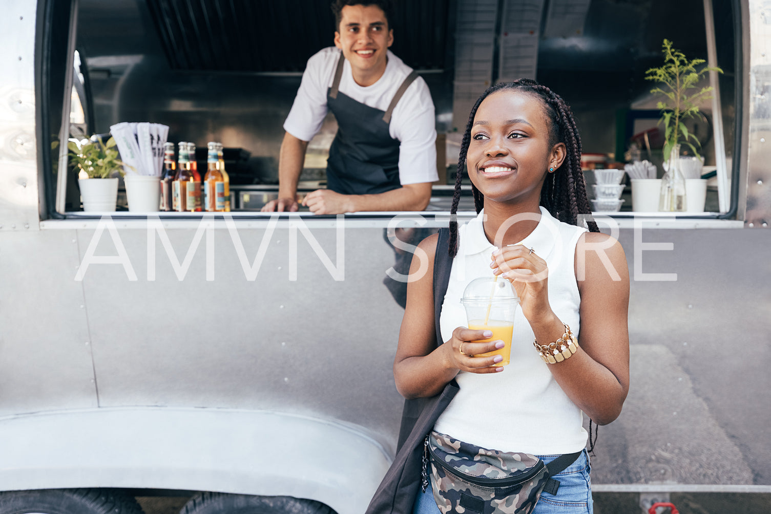 Smiling female customer holding orange juice against food truck with the owner