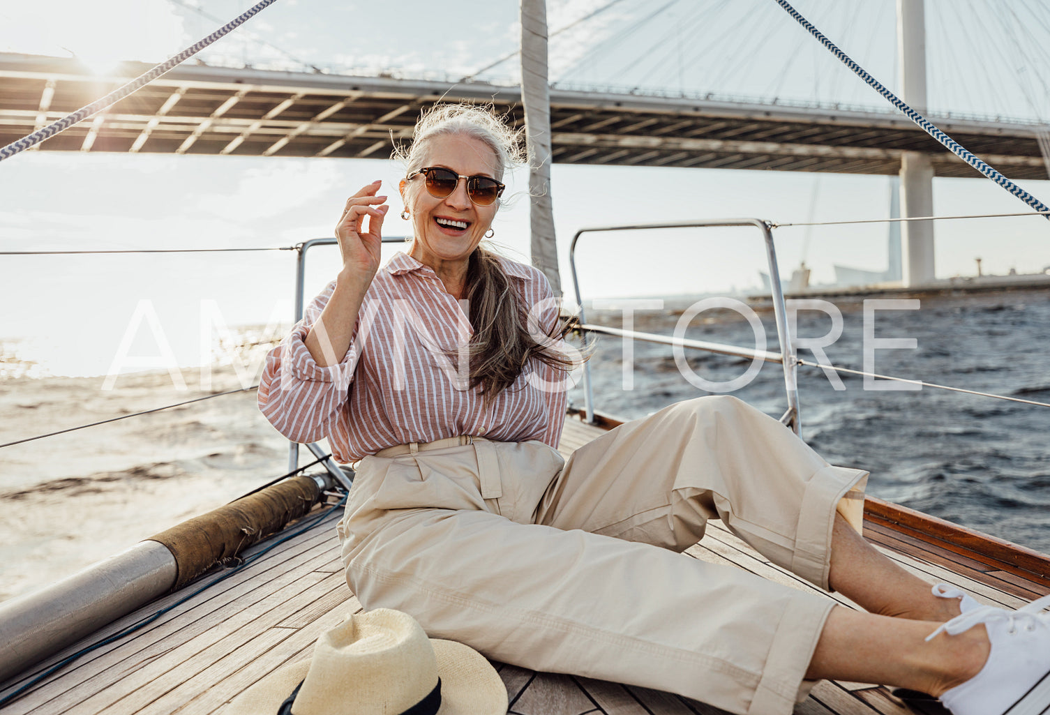 Happy mature woman resting on a yacht bow. Smiling female enjoying boat trip wearing sunglasses.	