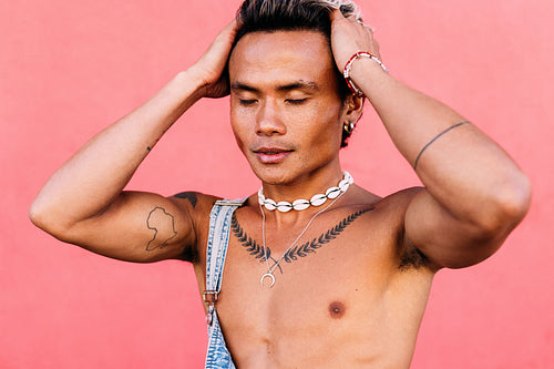 Close up of a young man with tattoos standing against pink wall with closed eyes