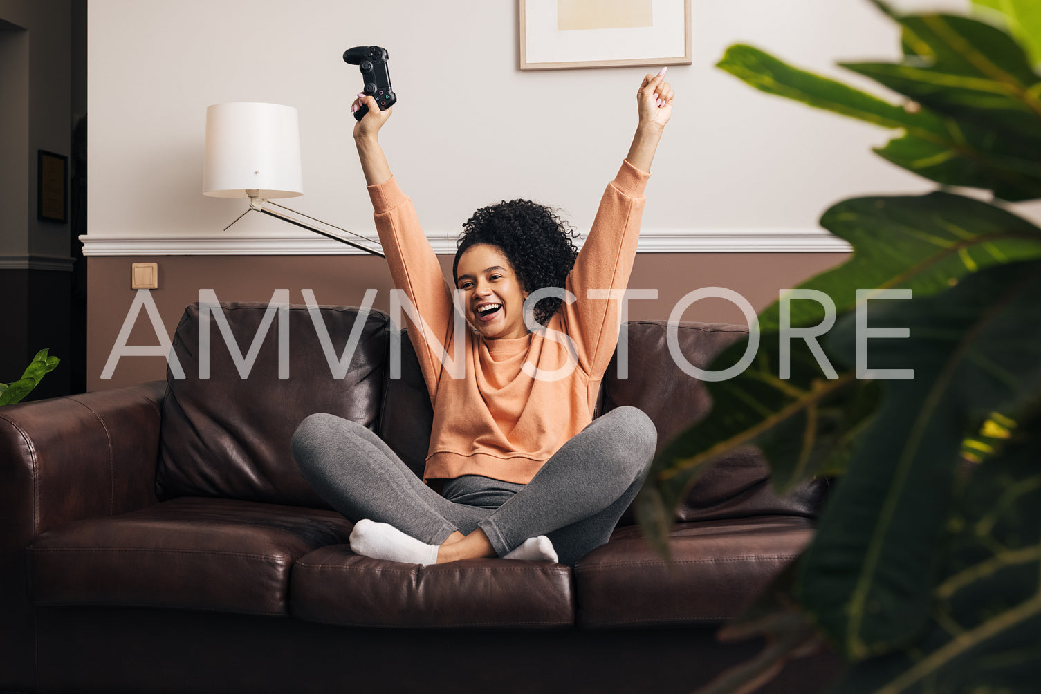 Happy mixed race woman sitting on a sofa in living room with raise hands up and holding a joystick