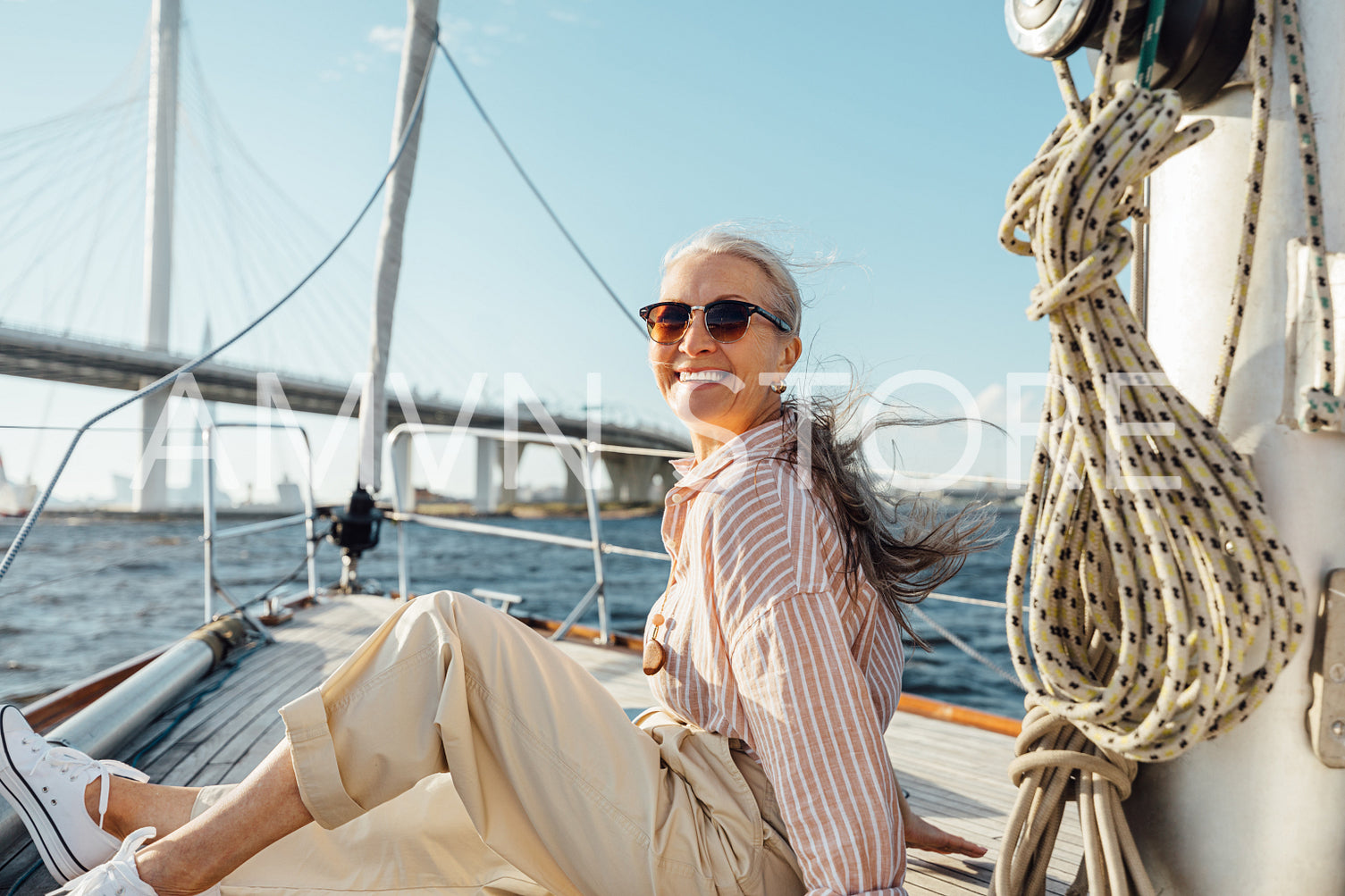 Happy mature woman wearing sunglasses on a sailboat and looking at camera. Senior female sitting on yacht deck and enjoying the voyage.	