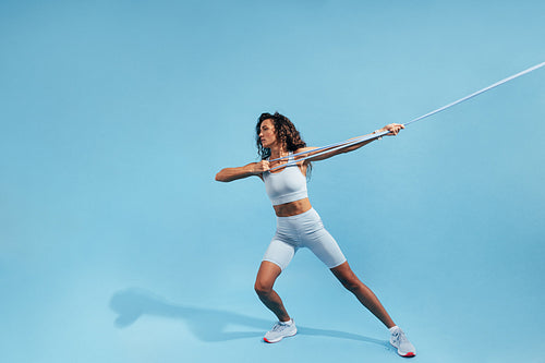 Muscular woman pulling resistance band. Young female in sportswear doing intense exercises with elastic band.