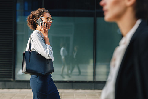 Woman carrying bag walking on city street to the office and making a call