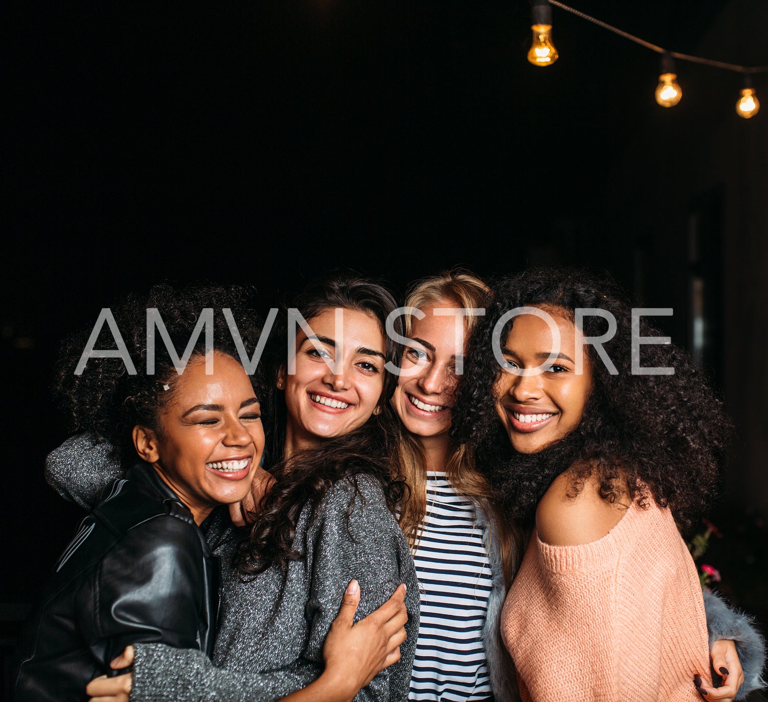 Group of four laughing female friends embracing at night