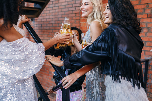 Group of women having drinks together. Female friends toasting with beer bottles while walking in the city.