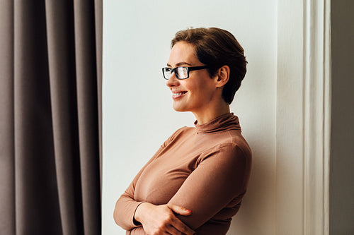 Side view of a beautiful businesswoman in eyeglasses standing in hotel room and looking at window