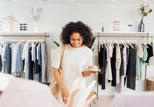 Stylish woman in boutique choosing belt. Young female standing in a local clothing store looking for accessories.