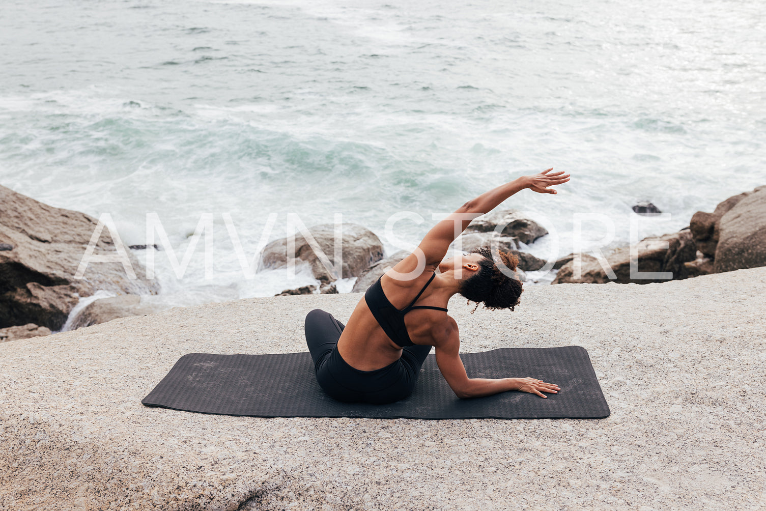 Muscular woman stretching on mat by ocean. Fit female doing flexibility exercises at seaside.