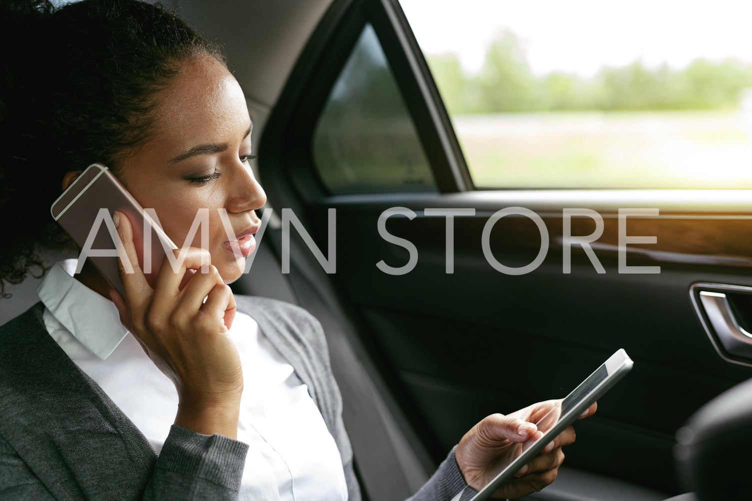 Businesswoman talking on a phone and using digital tablet, sitting on a backseat car	