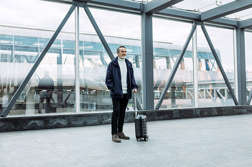 Man with suitcase standing in terminal. Aged tourist with baggage.