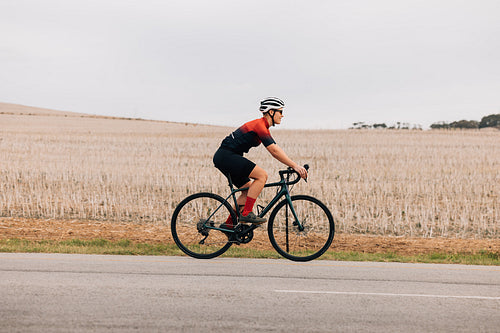 Side view of a female cyclist riding bike against field