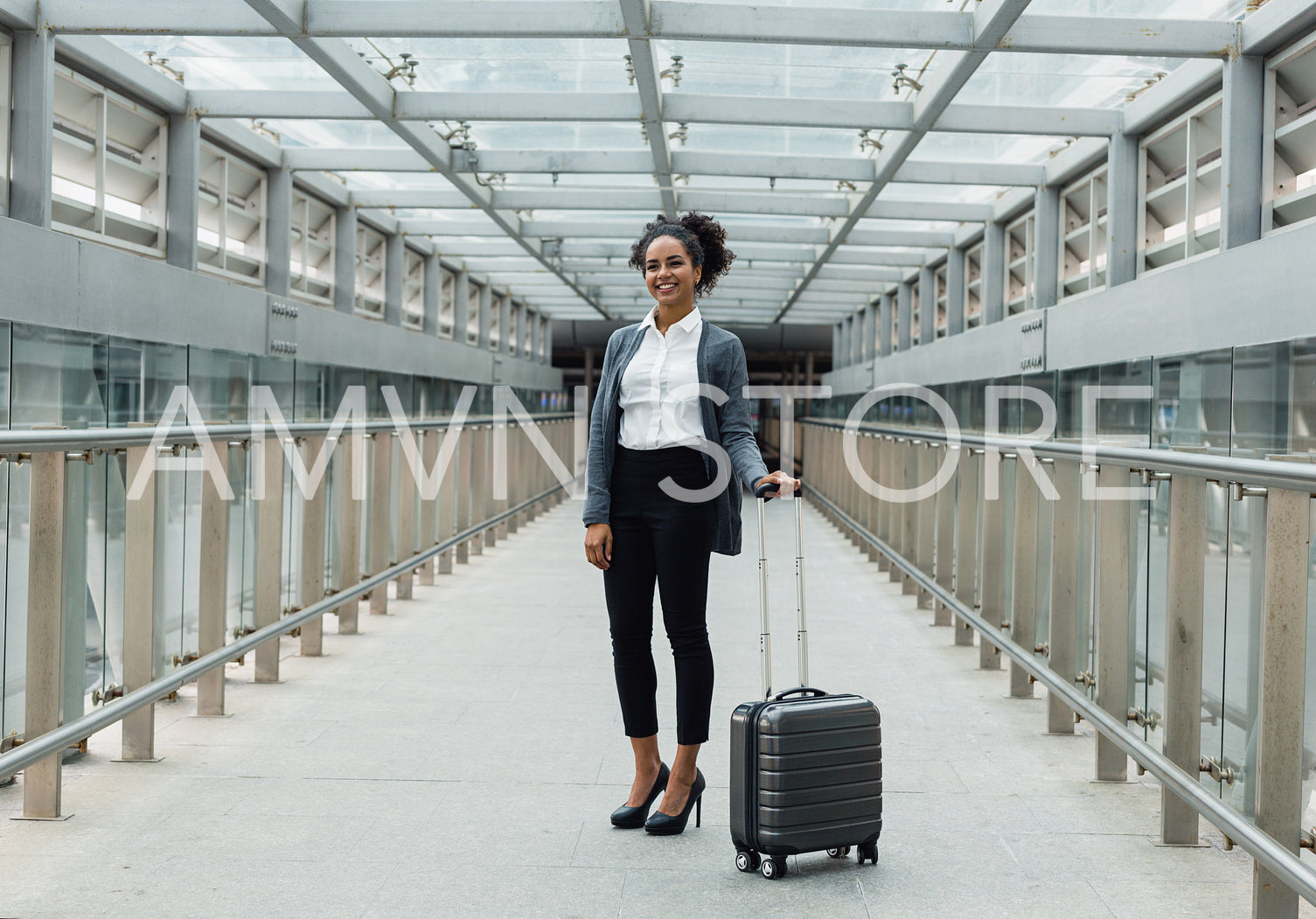 Smiling woman standing with suitcase in a center of corridor in transportation terminal	