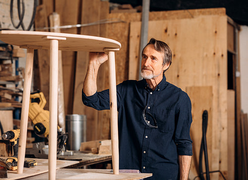 Senior carpenter standing at workbench and looks at the table he made