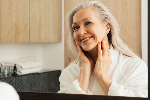 Cheerful aged female looking at her reflection in the morning