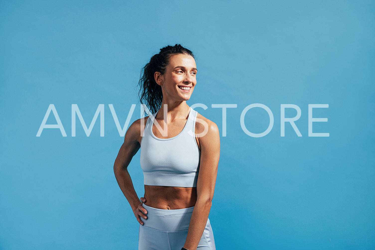 Portrait of a young smiling female in sportswear posing on blue background 