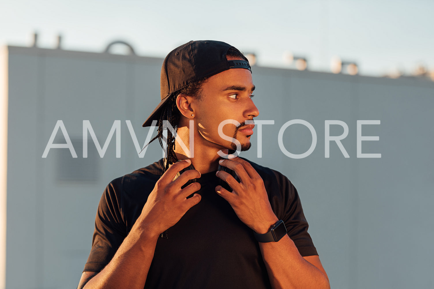 Young male athlete with dreadlock wearing a black hat looking away 