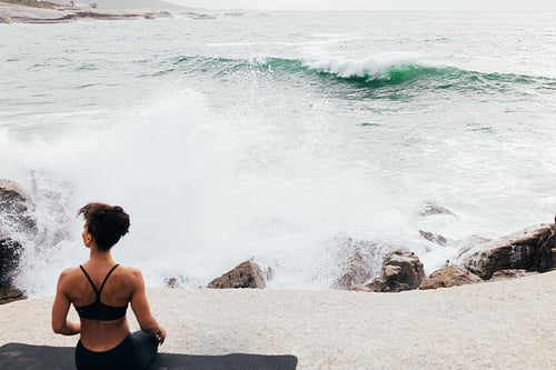 Selective focus shot of a woman sitting on a mat against ocean at sunset