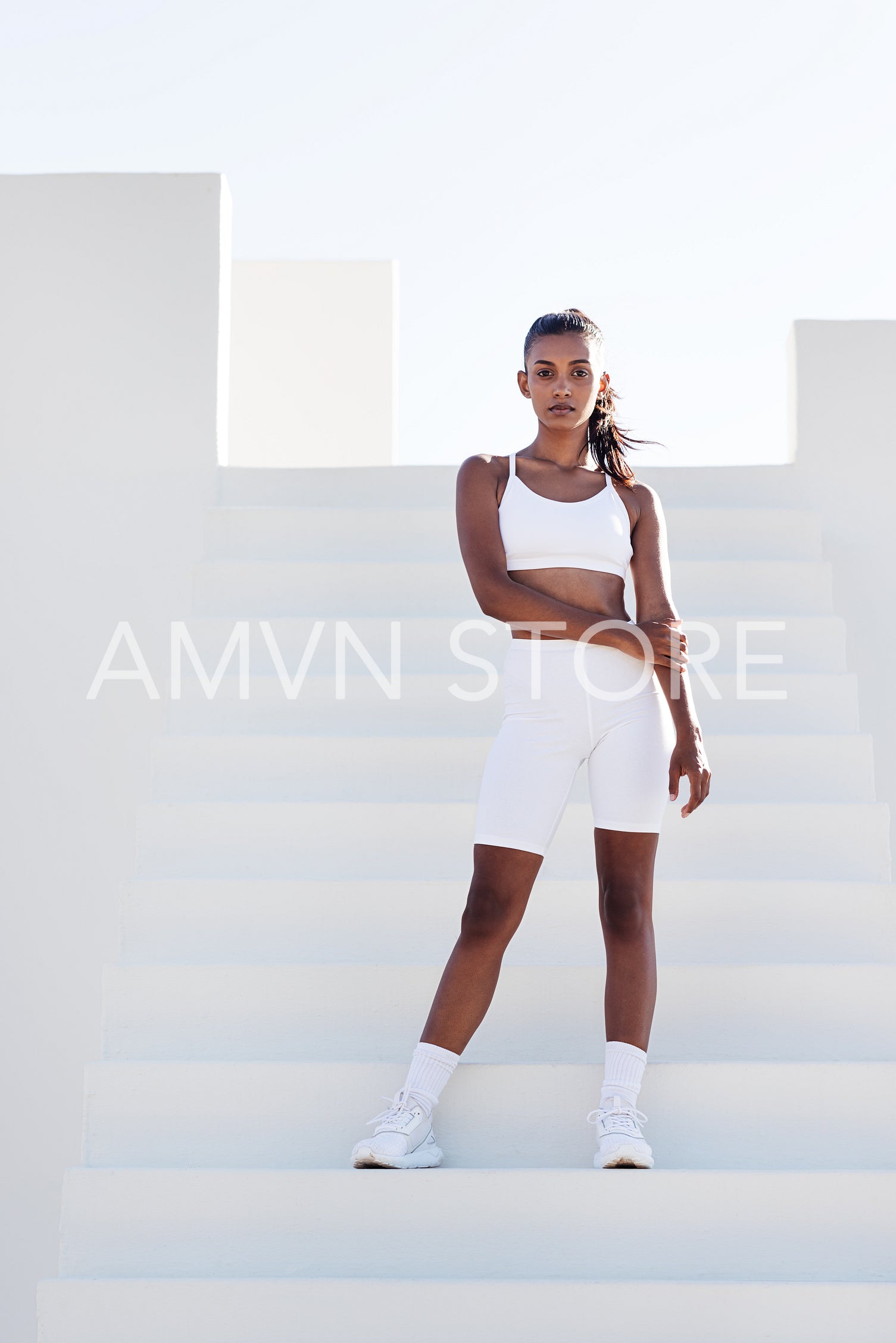 Full-length slim fit female in white sports attire. Woman standing on white stairs relaxing during training.