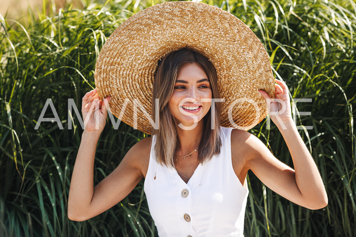 Beautiful happy woman sitting in a park and holding her straw hat