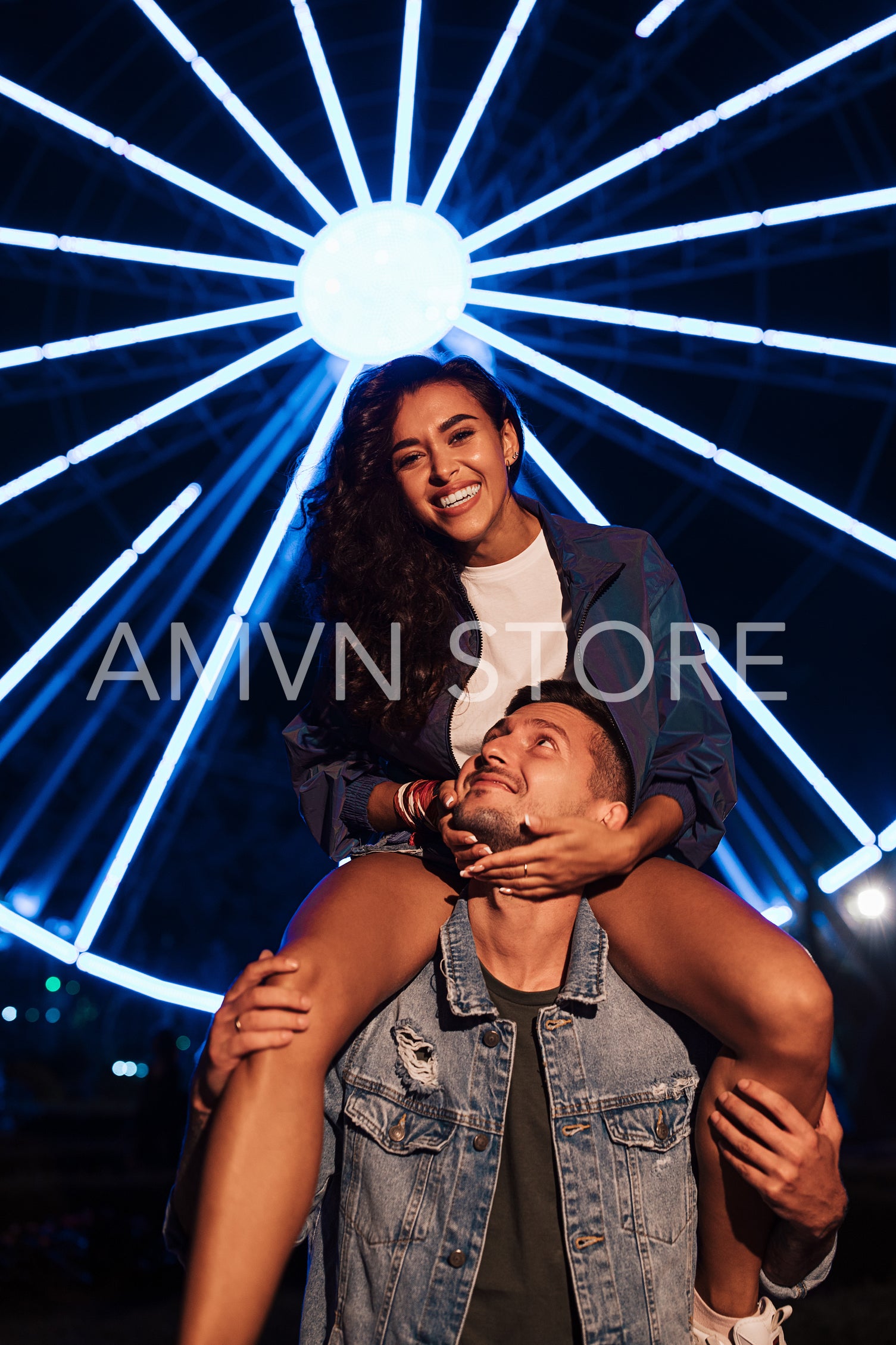 Young woman looking at camera against lights of ferris wheel. Couple at night during the festival.