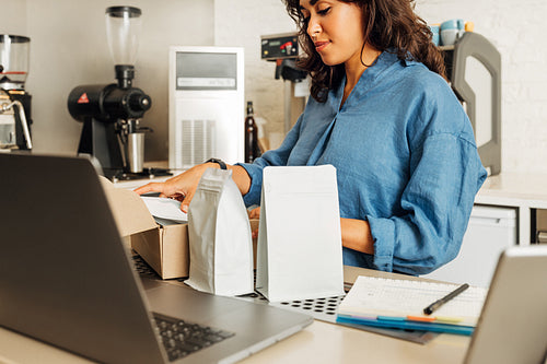 Woman working in her small cafe puts packs of coffee in a delivery box. Business owner preparing parcel.