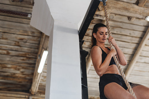 Strong determined woman climbing rope at gym