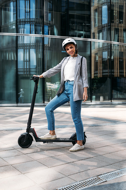 Young cheerful woman standing in the city with electric push scooter