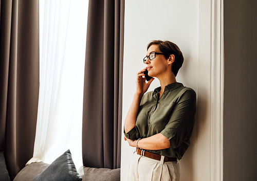 Businesswoman standing near in hotel room window and making a phone call