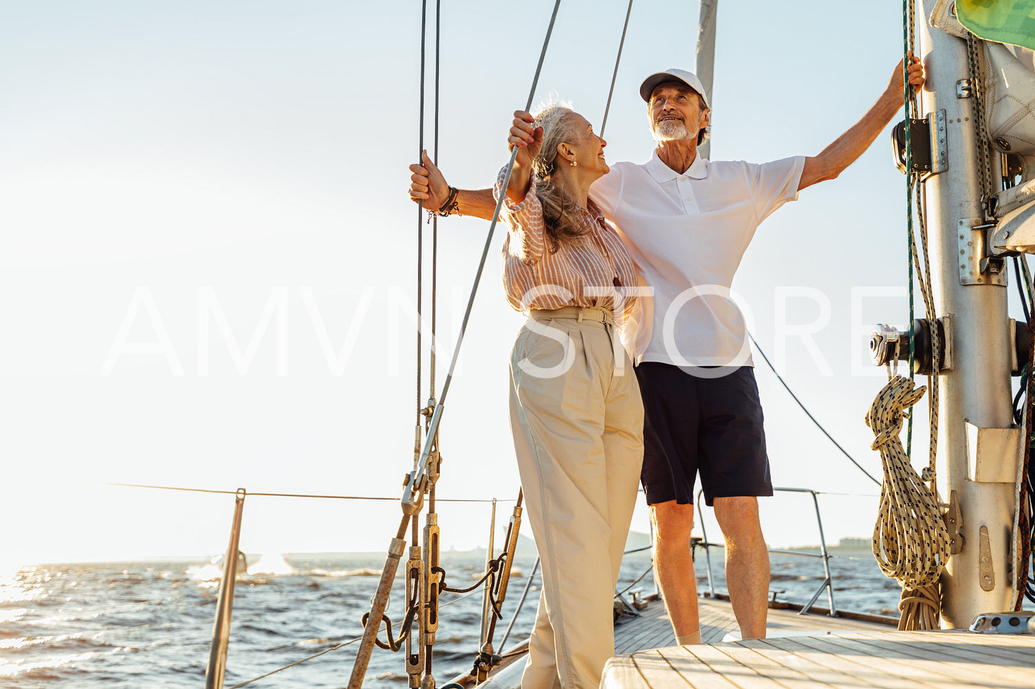 Elderly people standing on private sailboat and holding ropes	