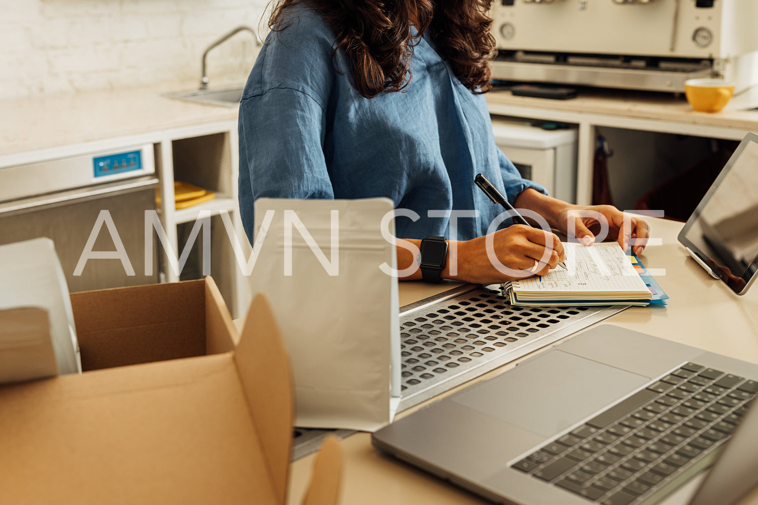 Mid section of businesswoman in her small cafe writing on notebook. Entrepreneur preparing packs of coffee for shipment.	