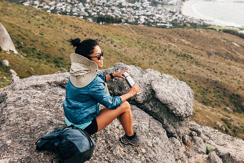 Woman hiker relaxing during hike sitting on a stone holding thermos