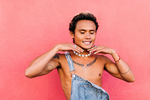 Portrait of a young smiling guy having fun with closed eyes while standing at pink wall