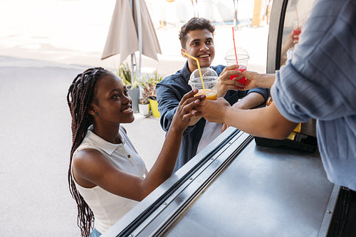 Two smiling customers receiving juice from unrecognizable saleswoman at a food truck