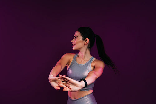 Slim woman in silver fitness wear doing warming-up exercises against a magenta background