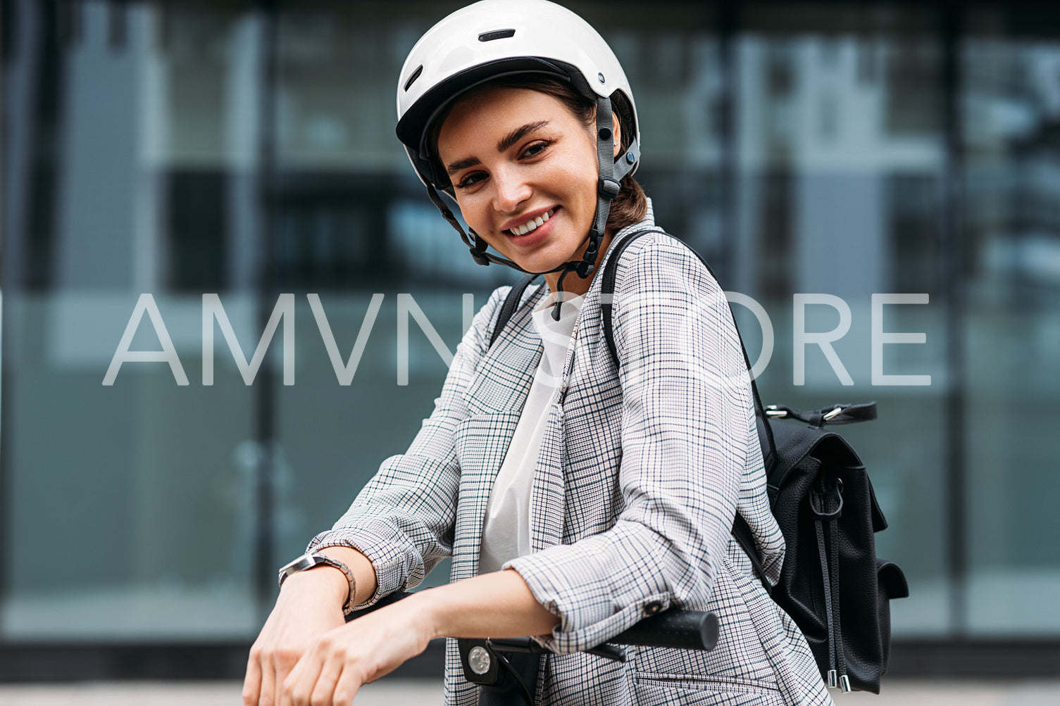 Portrait of cheerful businesswoman in white cycling helmet looking at camera leaning on handlebar of electric push scooter