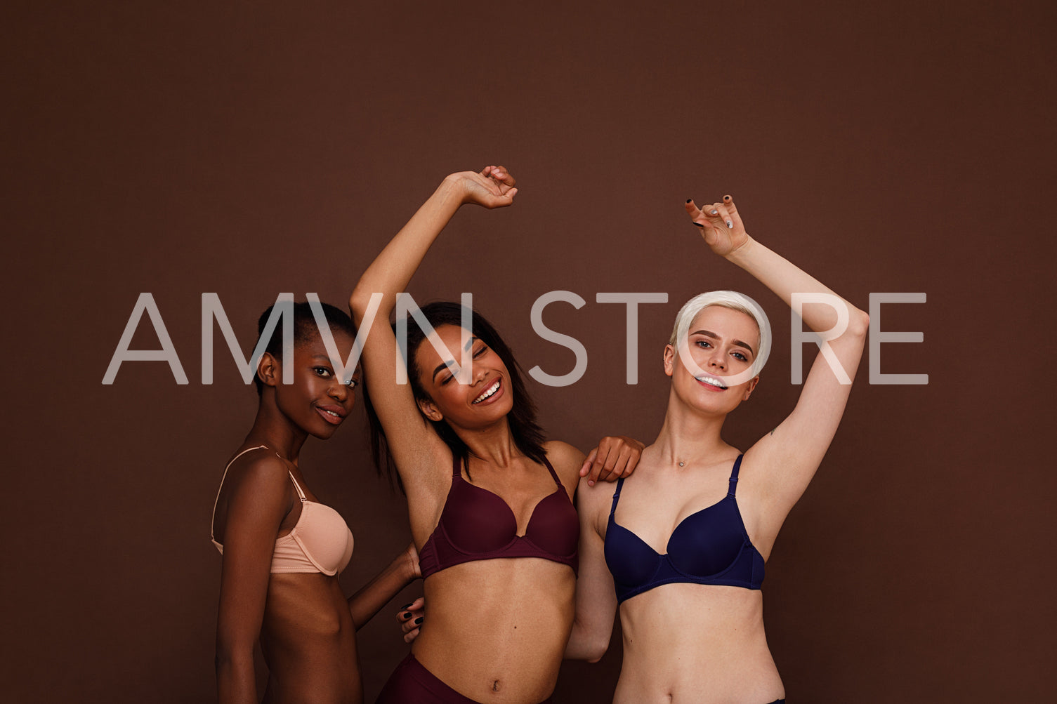 Three women in lingerie are laughing. Females in underwear dancing against a brown backdrop.