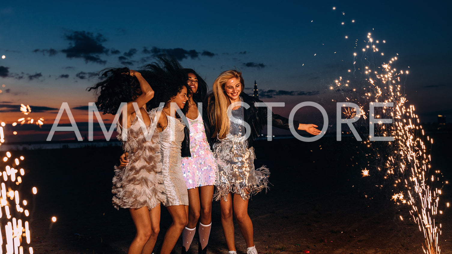 Group of happy girlfriends dancing between fireworks at night. Young stylish women celebrating at sunset.	