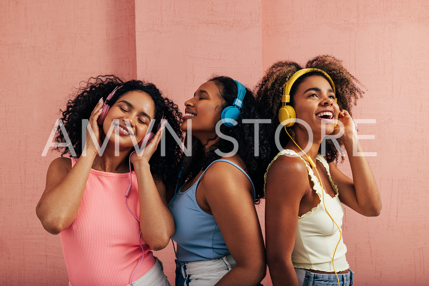 Three beautiful women standing together and listening to music. Girlfriends with headphones wearing bright casual clothes enjoying good mood and music.