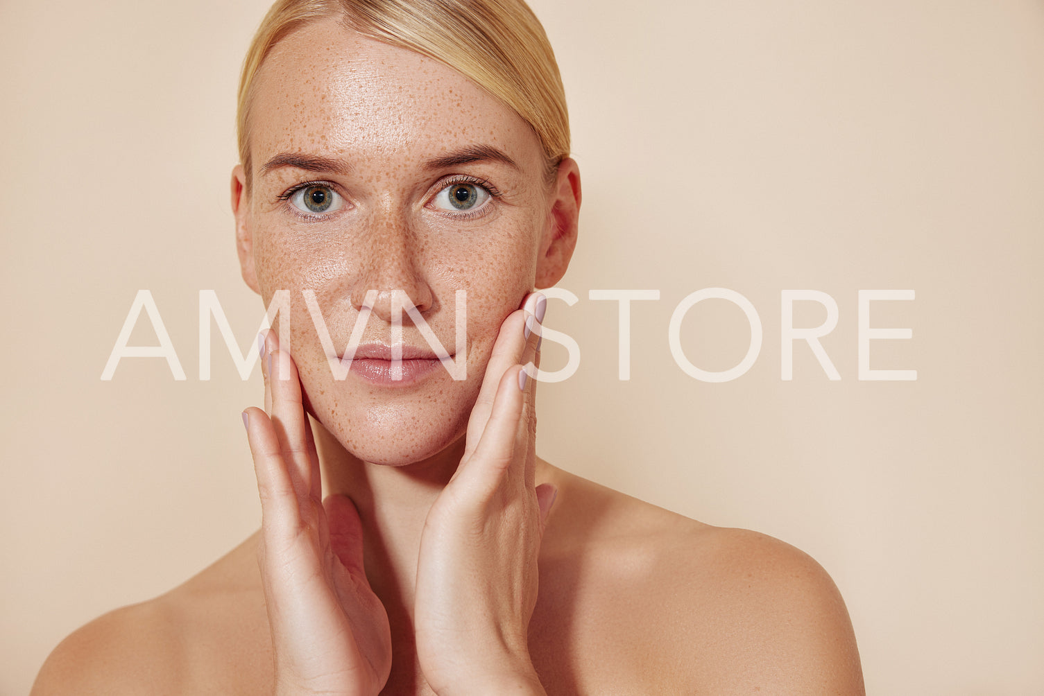 Female with freckled skin touching her face. Portrait of a beautiful blond woman looking at the camera and massaging her face.