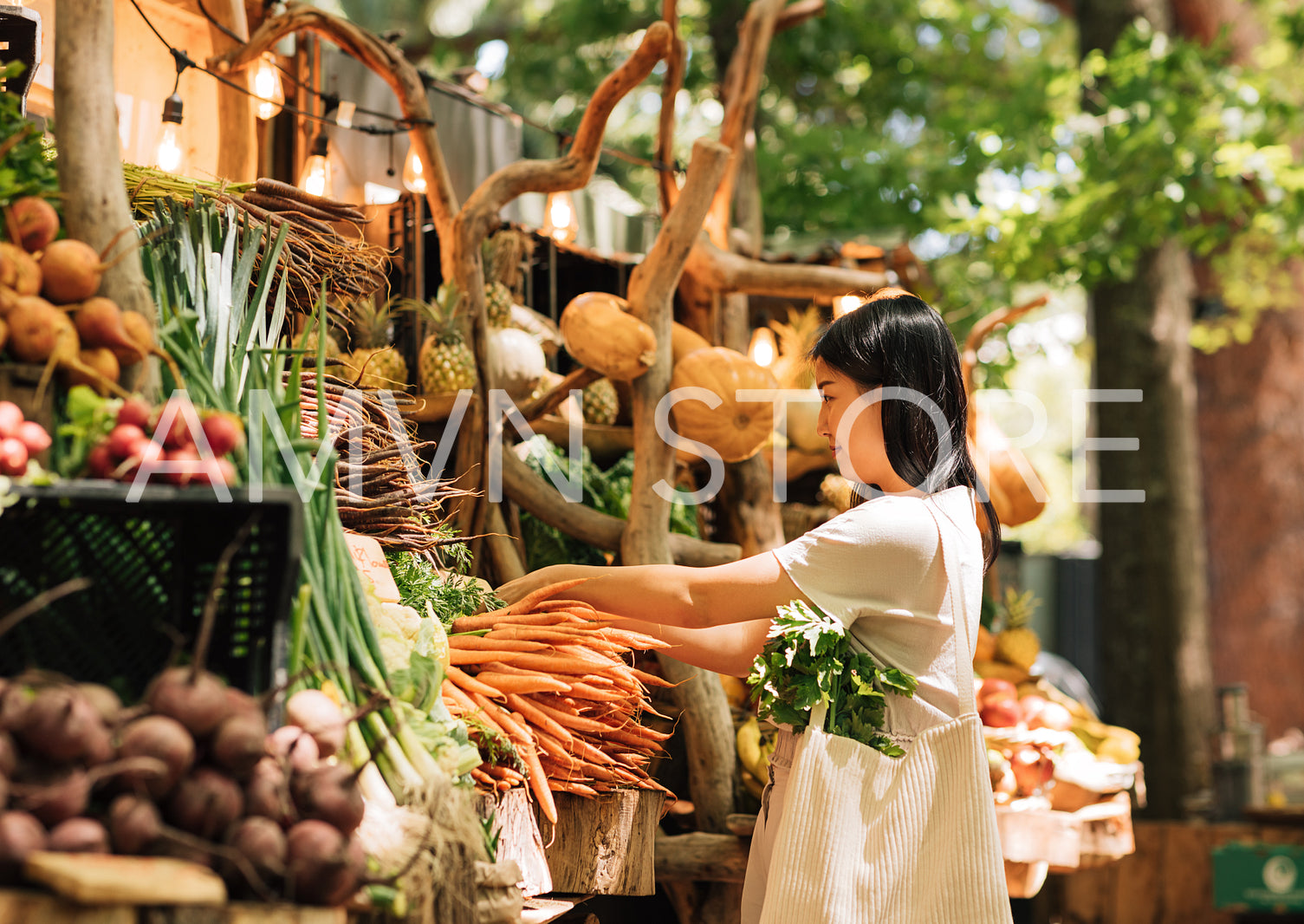 Side view of a young woman in an outdoor market. Female with shopping bag buying fresh vegetables.