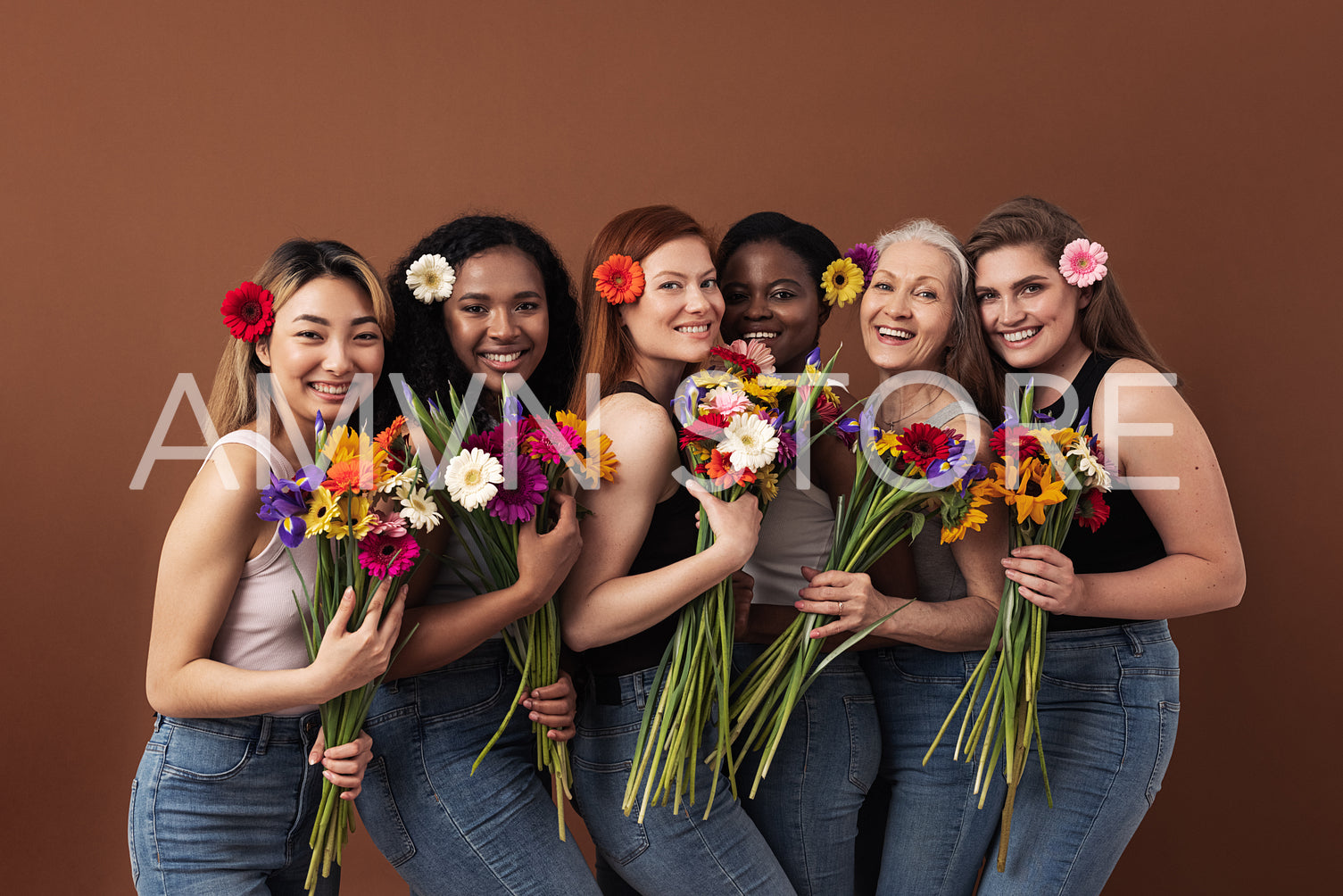 Six smiling women of different ages looking at camera in a studio. Happy diverse females with bouquets and flowers in their hairs standing together.