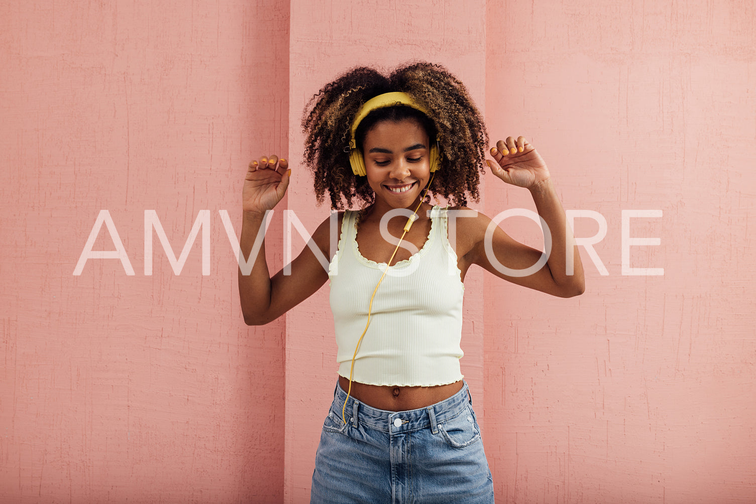 Cheerful woman in yellow headphones enjoying music raising hands