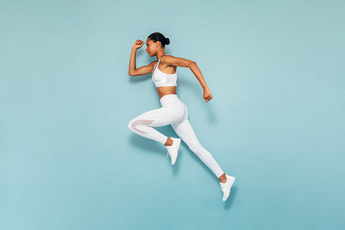 Sports woman running in studio. Full length shot of young female exercising over blue backgroud.