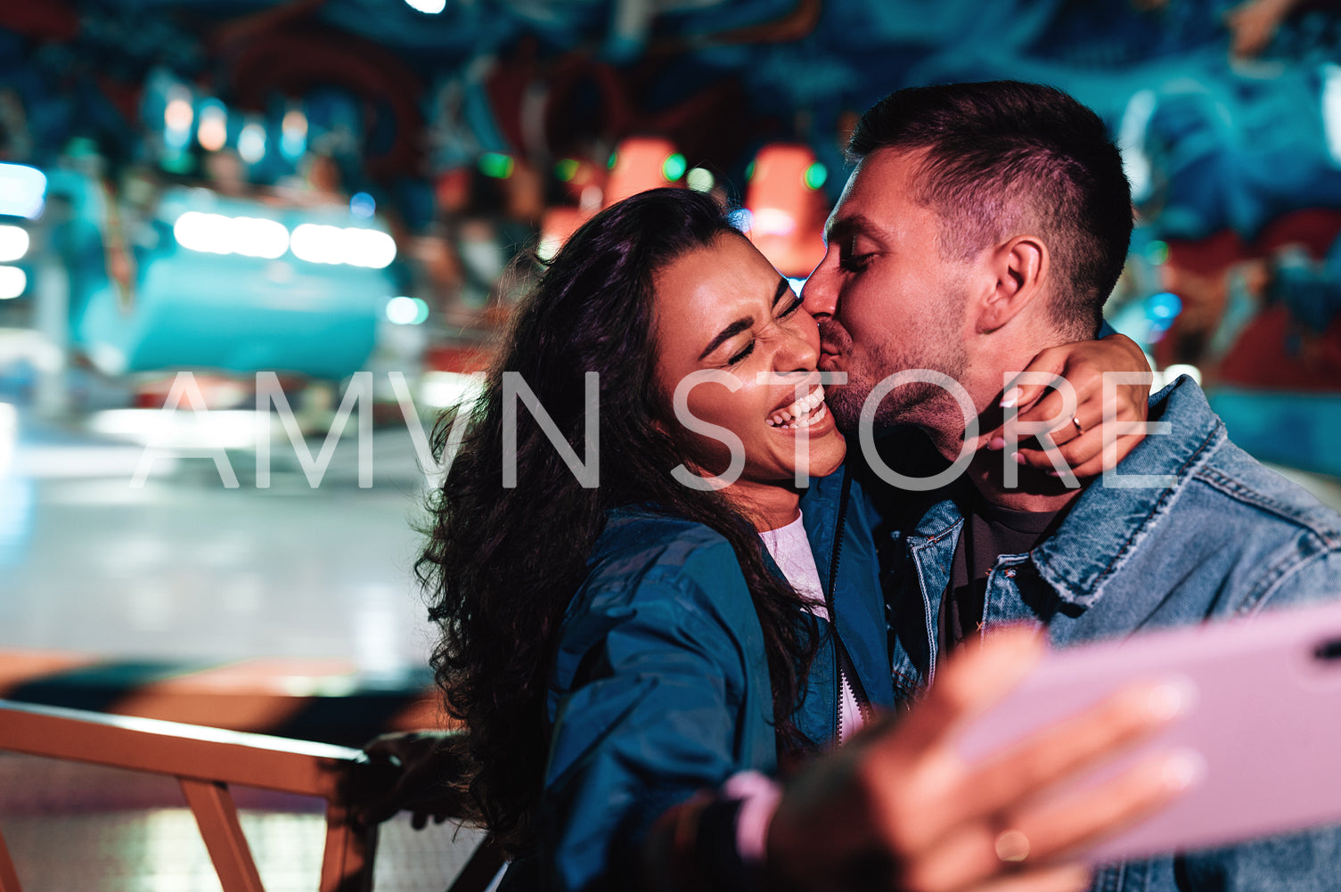 Boyfriend kissing his girlfriend while she is making selfie. Young couple during a summer festival.