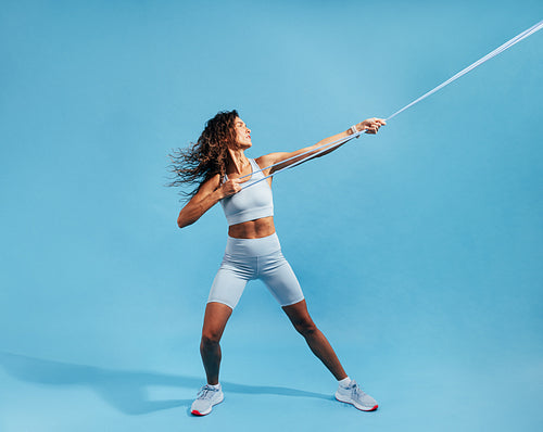 Muscular sportswoman exercising with resistance band on blue background. Female working out with elastic band.