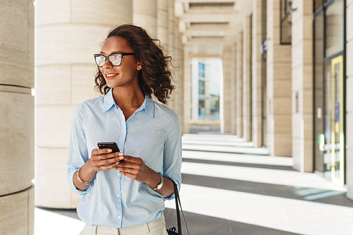 Smiling woman holding a cell phone with office building on background